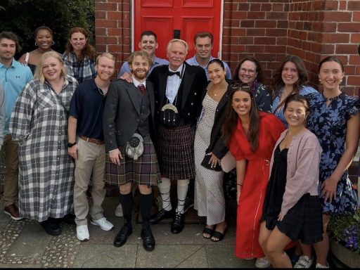 Photo of Campbell Law students surrounding Dean Rich Leonard wearing traditional Scottish kilt in front of a red door in Scotland
